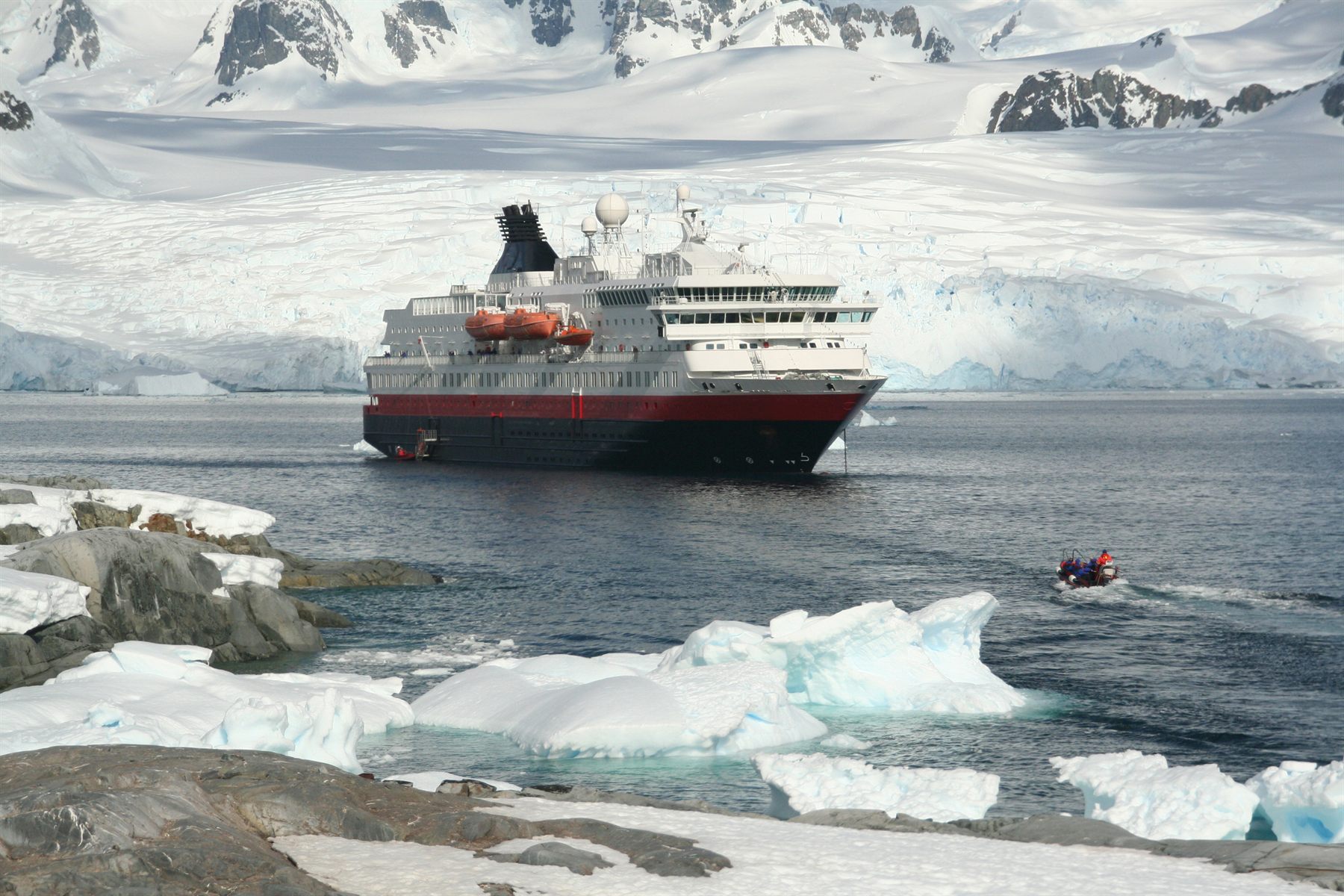 A red-and-white expedition ship among sea ice below snowy Antarctic mountains